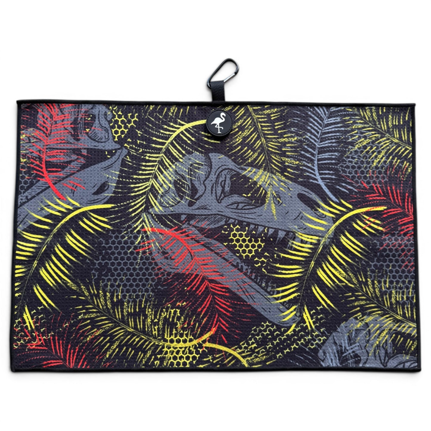 The Jurassic Fairway Golf Towel (24” x 16”) is a rectangular microfiber towel with a black background, red/yellow/gray tropical leaves, black border, hanging loop, white animal logo tag at top center, plus magnetic clip and carabiner.
