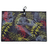 The Jurassic Fairway Golf Towel (24” x 16”) is a rectangular microfiber towel with a black background, red/yellow/gray tropical leaves, black border, hanging loop, white animal logo tag at top center, plus magnetic clip and carabiner.