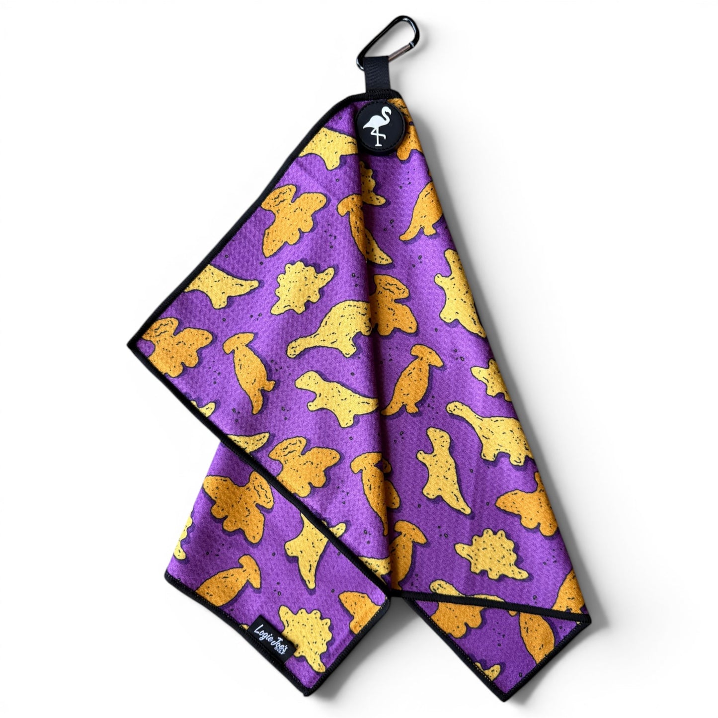 The Purple Dino Chicken Nugget Golf Towel is a 24” x 16” microfiber towel with a yellow dinosaur pattern, black trim, flamingo logo tag, and includes both a magnetic clip and carabiner for easy attachment.