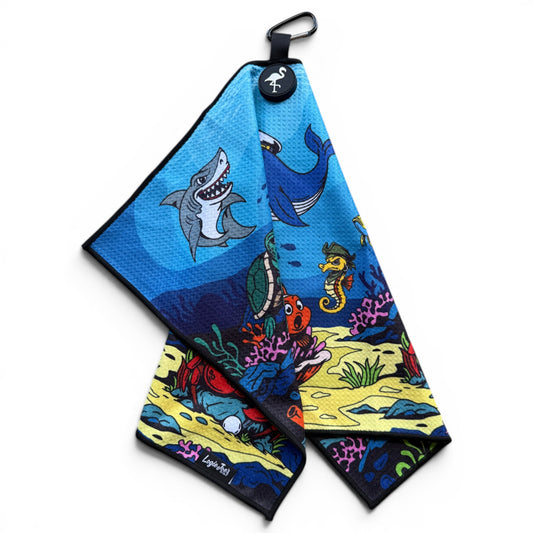 The Deep Blue Sea Golf Towel (24” x 16”) is a colorful microfiber towel with cartoon sea animals on a blue background, featuring a magnetic clip, carabiner, and round logo in the corner—perfect as a premium golf accessory.