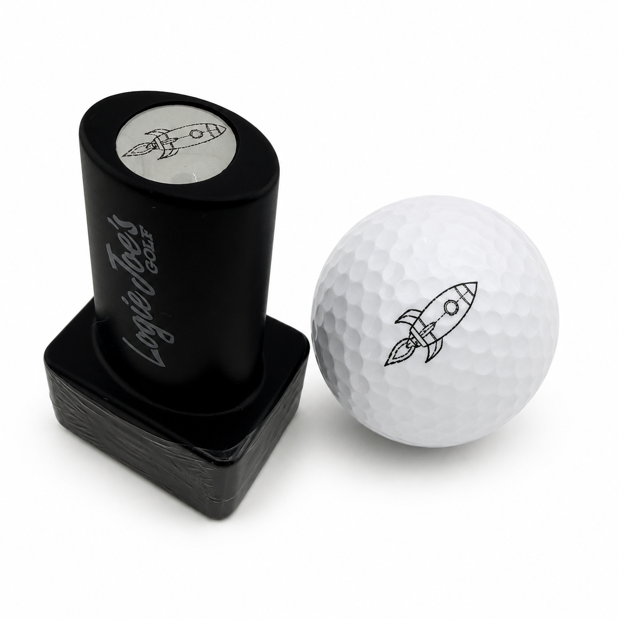 A black Pocket Rocket Stamp with quick-dry ink sits beside a white golf ball marked by the same rocket design, making ball identification easy and adding fun to your game.