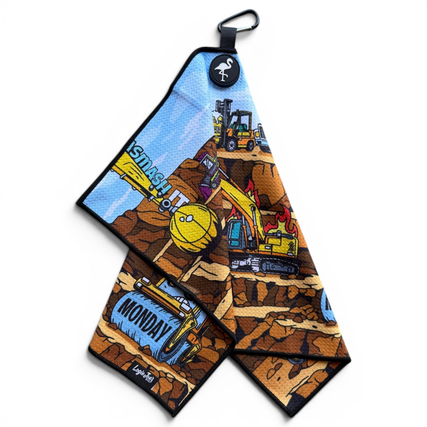 The Wrecking Crew Golf Towel (24” x 16”) features cartoon construction vehicles on a dirt background, playful “MONDAY” text, animated faces, and comes with a magnetic clip and carabiner for easy attachment.