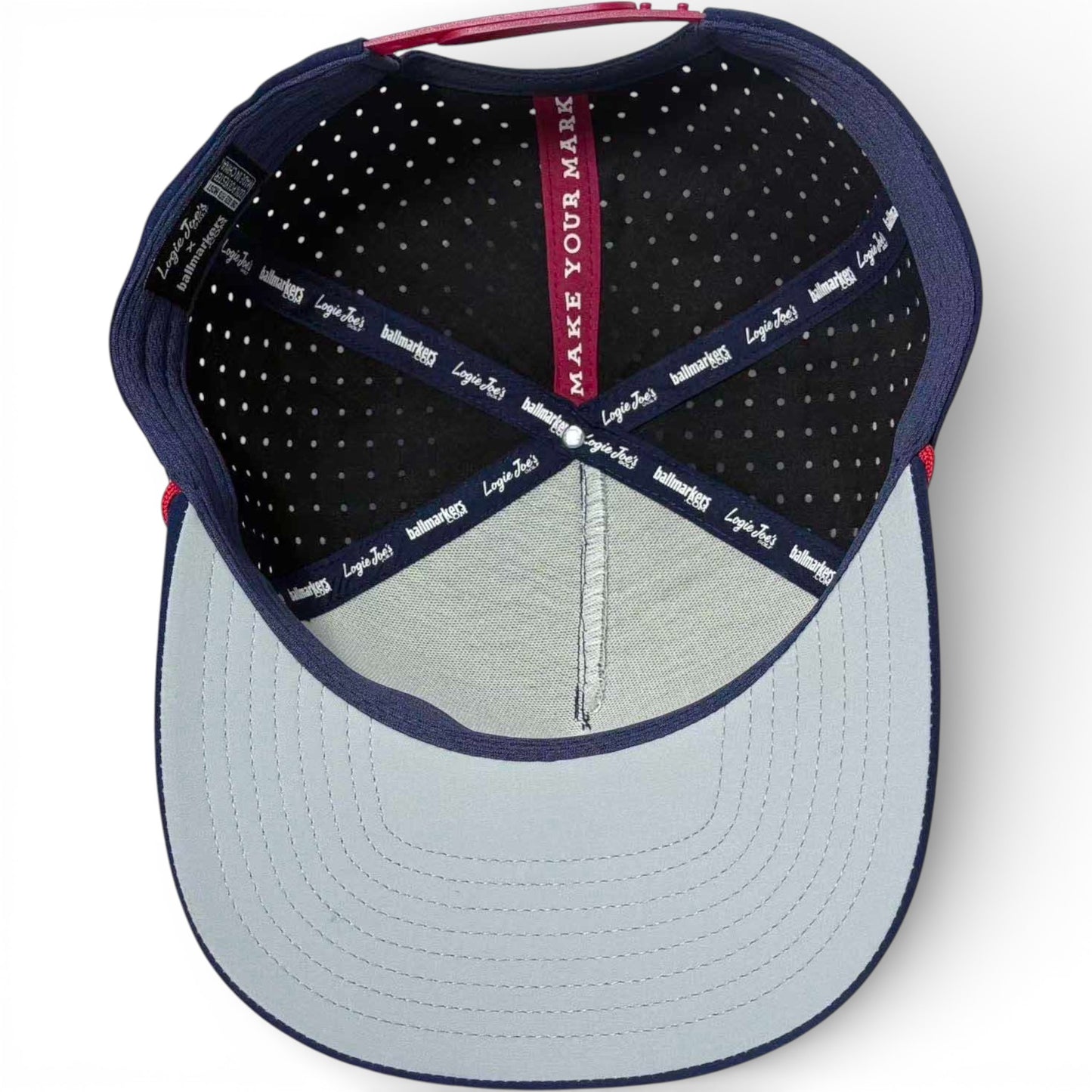 The inside of the Crab Trap Golf Hat Snapback Cap features a light blue brim, black polka-dot lining, navy-blue trim, and a red MAKE YOUR MARK strip with logo text on the adjustable inner band. Includes built-in magnetic ball marker holder and marker.