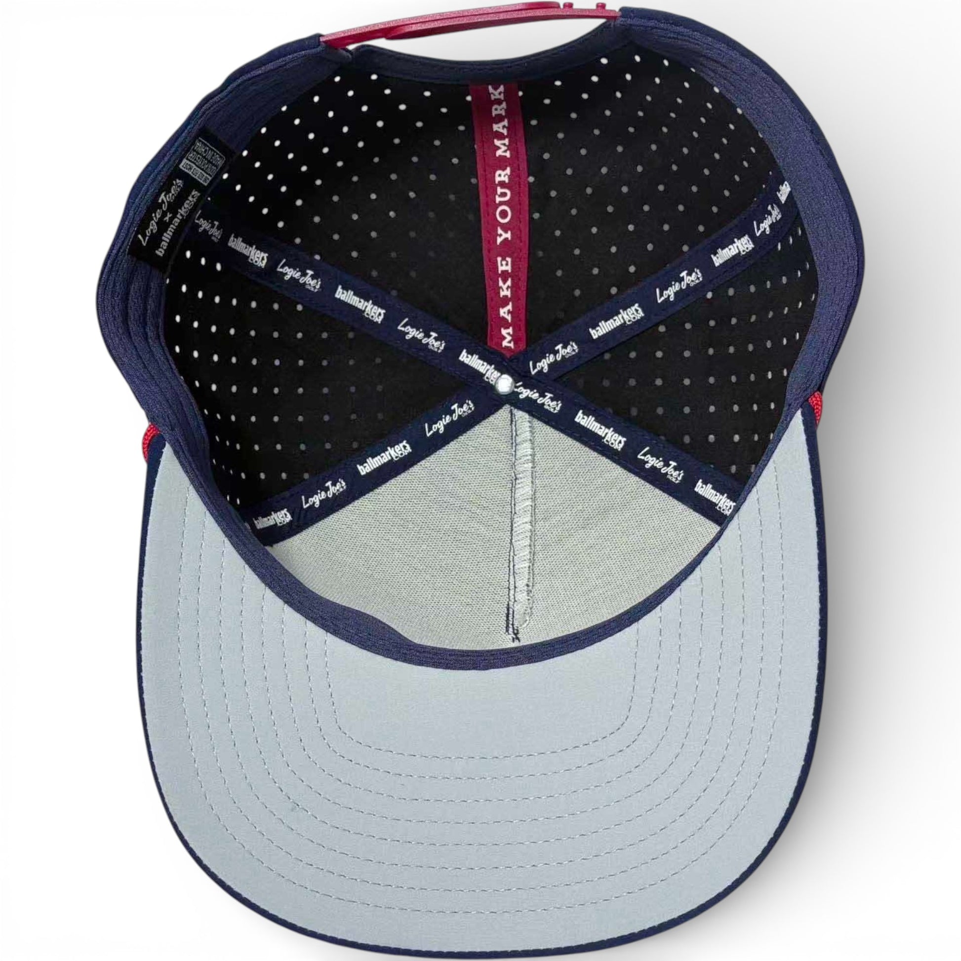 The inside of the Crab Trap Golf Hat Snapback Cap features a light blue brim, black polka-dot lining, navy-blue trim, and a red MAKE YOUR MARK strip with logo text on the adjustable inner band. Includes built-in magnetic ball marker holder and marker.