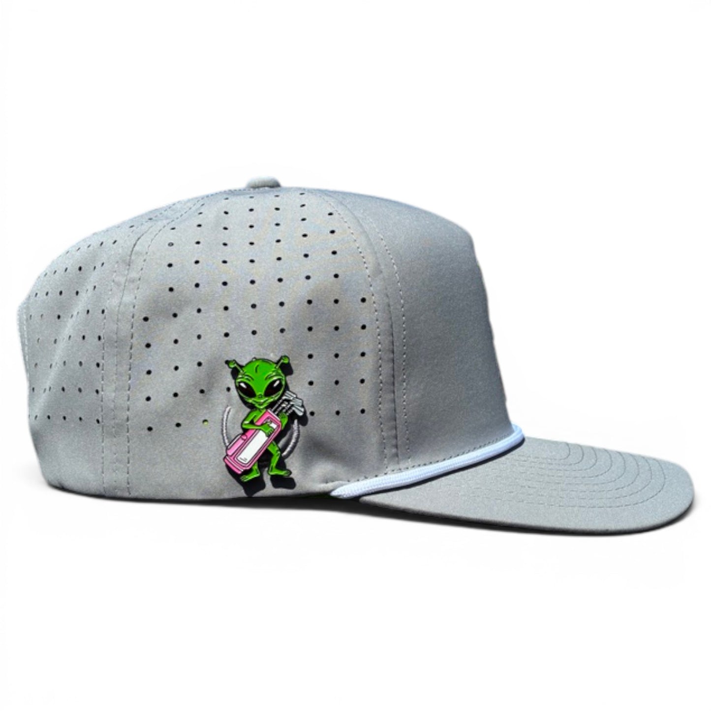 The Alien Caddy Golf Hat is a light gray adjustable snapback cap with a white-trimmed visor, built-in magnetic ball marker holder and marker, and features a green alien with a pink boombox on the side. Displayed against a white background.
