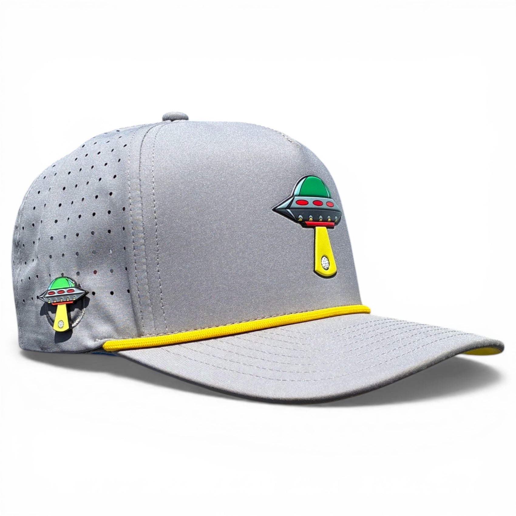 The Alien Gray UFO Golf Hat is a snapback cap with yellow trim, green and black UFO graphics beaming up a golf ball, ventilation holes for breathability, built-in magnetic ball marker holder, marker included, and adjustable fit.