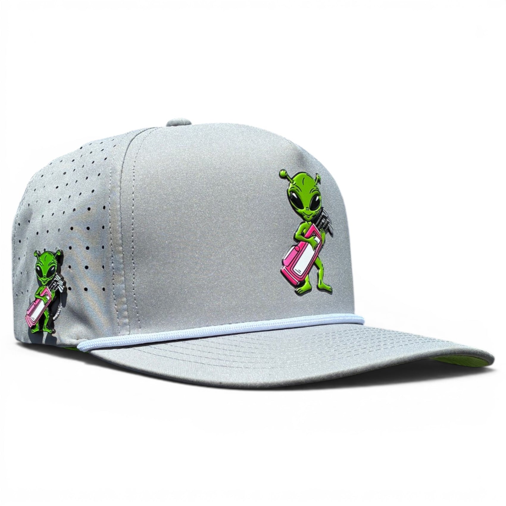 The Alien Caddy Golf Hat is a light gray snapback cap featuring a cartoon green alien with a pink and white golf bag, ventilation holes, curved brim, adjustable fit, and a built-in magnetic ball marker holder with marker included.