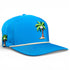 The Fairway Palms Golf Hat is a bright blue adjustable snapback with cartoon palm tree and coconut graphics, beige rope detail, ventilation holes, and a built-in magnetic ball marker holder. Marker is included; one size fits most.