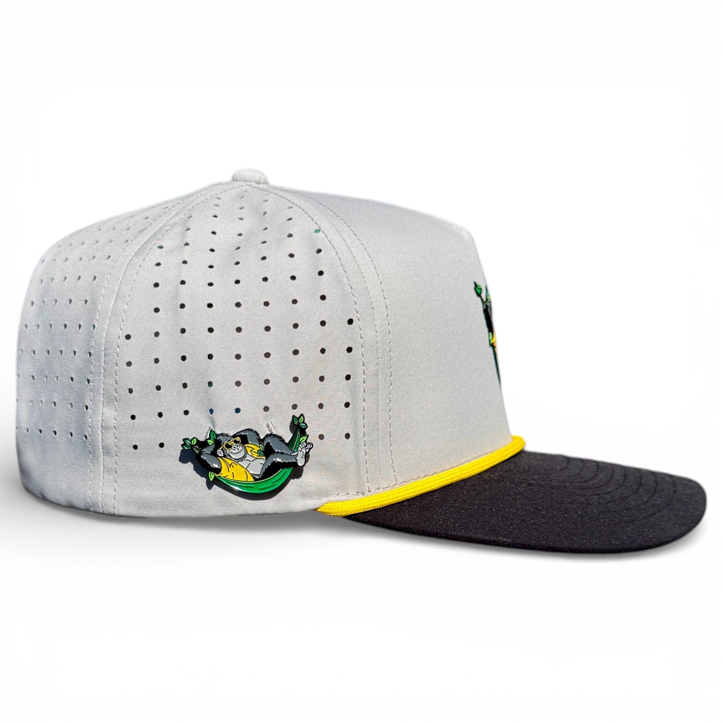 The Banana Hammock Golf Hat is a light gray snapback cap with small ventilation holes, black brim, yellow trim, and a cartoon lounging wizard; features an adjustable fit and built-in magnetic ball marker holder plus marker.