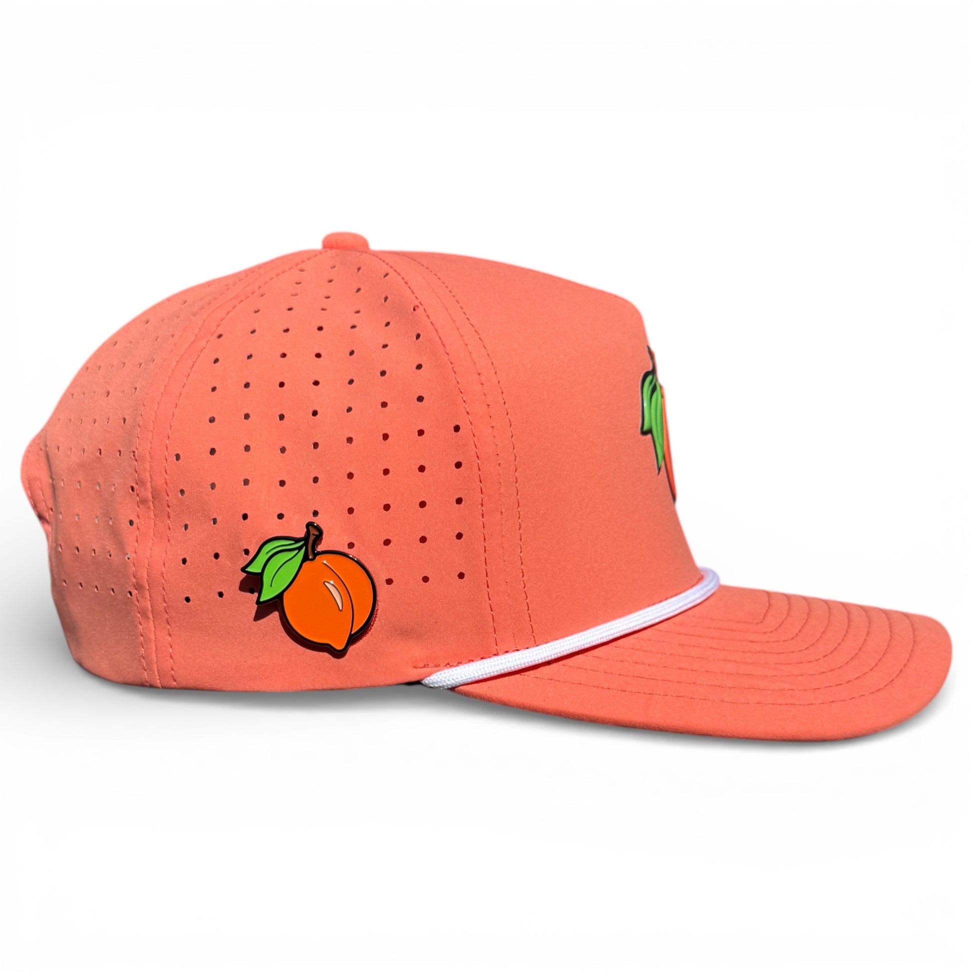 The Just Peachy Golf Hat is a coral-colored adjustable snapback cap with perforated sides, a peach and green leaves graphic, white brim accent, and features a built-in magnetic ball marker holder with marker included.