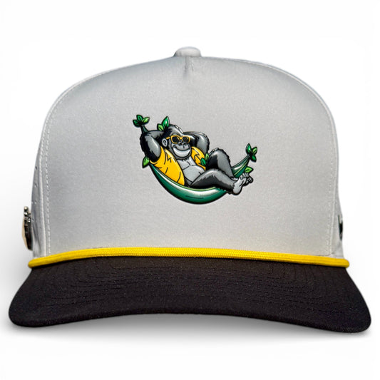 The Banana Hammock Golf Hat is a gray and black adjustable snapback cap with yellow trim, featuring an embroidered gorilla in sunglasses lounging in a green hammock, plus a magnetic ball marker holder and marker included.