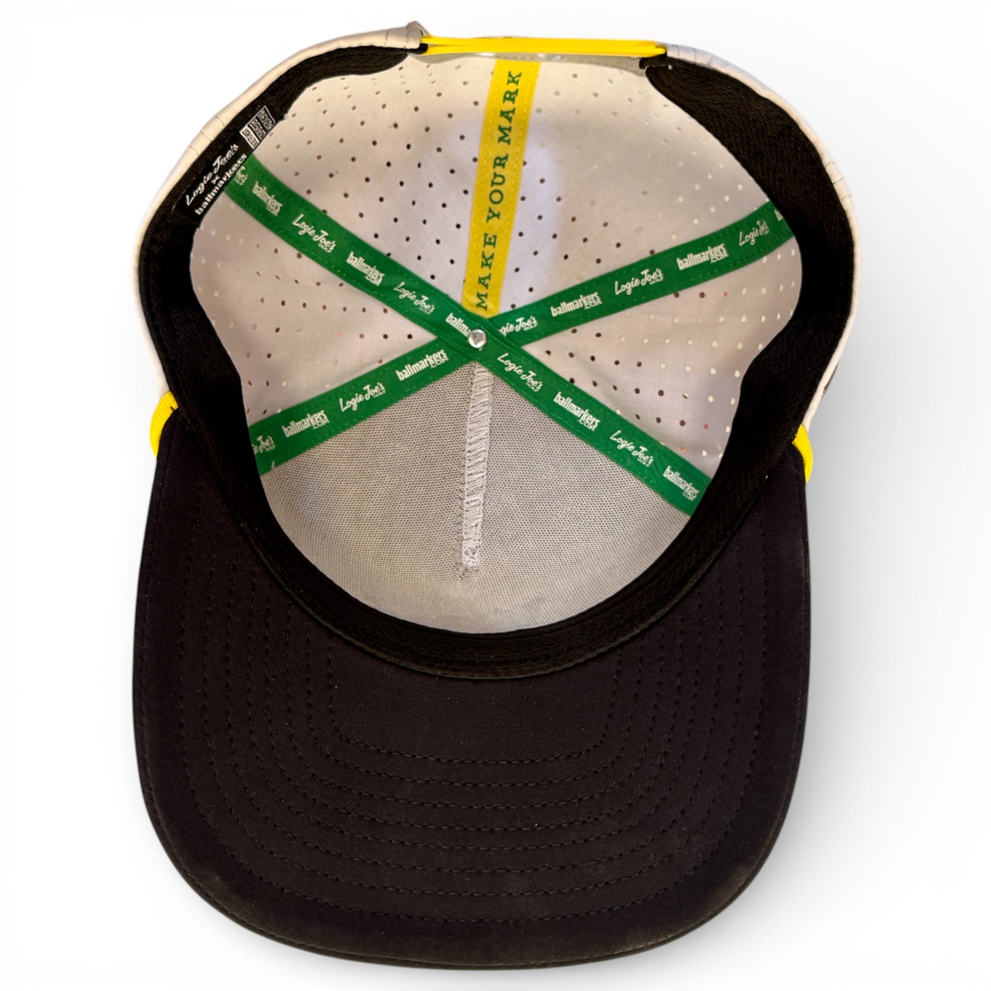 Inside view of the Banana Hammock Golf Hat, a black-brimmed snapback with green and yellow lining bands. Features "MAKE YOUR MARK" text, Lays x Sub logos, and a built-in magnetic ball marker holder with marker included. Adjustable, one size.