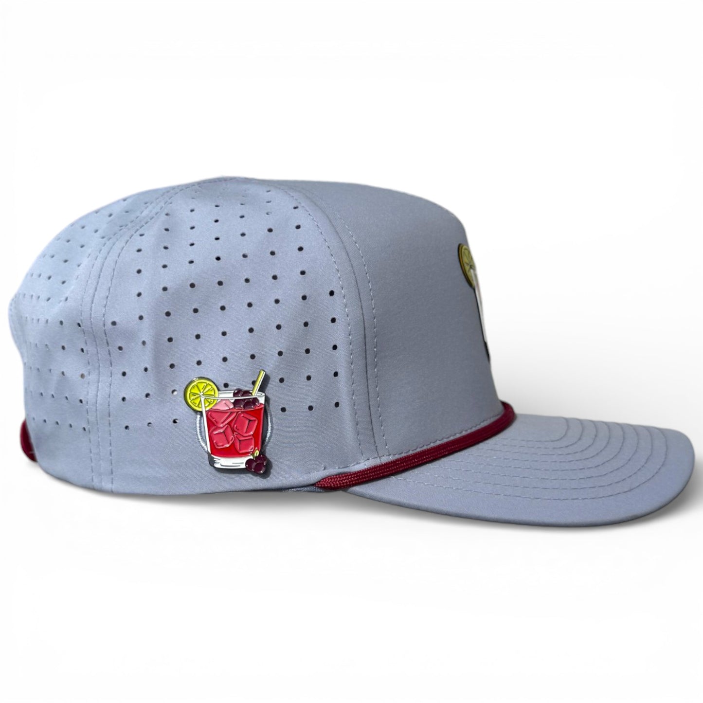 The Transfusion Golf Hat is an adjustable light gray snapback cap with maroon brim trim, a colorful red cocktail enamel pin, and a built-in magnetic ball marker holder with marker included.