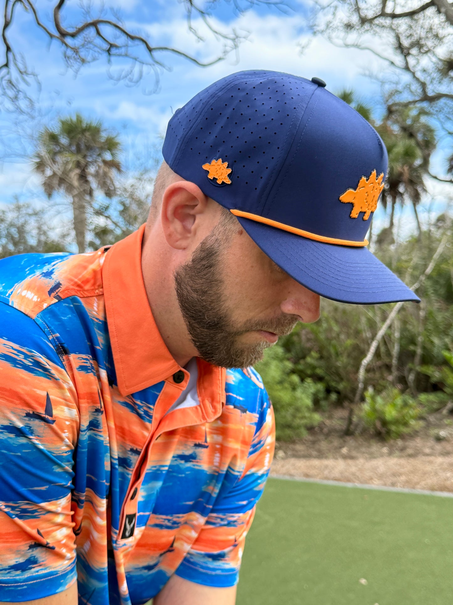 A man in a Dino Nugget Golf Hat—an adjustable snapback cap with a built-in magnetic ball marker holder and included marker—stands outdoors on the golf course, stylishly equipped for play.
