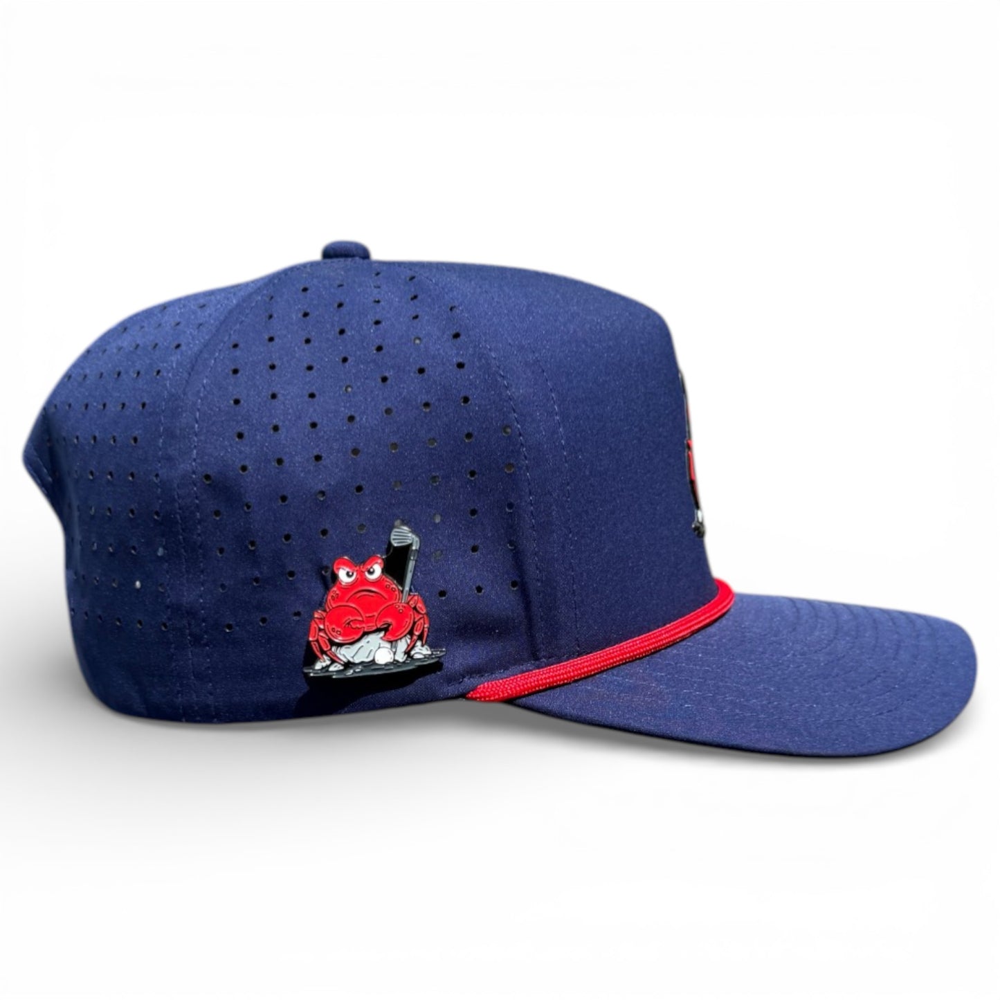 The Crab Trap Golf Hat is a navy blue adjustable snapback cap with red accents, featuring a red cartoon frog holding a baseball bat on the side. It has ventilation holes, a flat brim, and includes a built-in magnetic ball marker holder with marker.