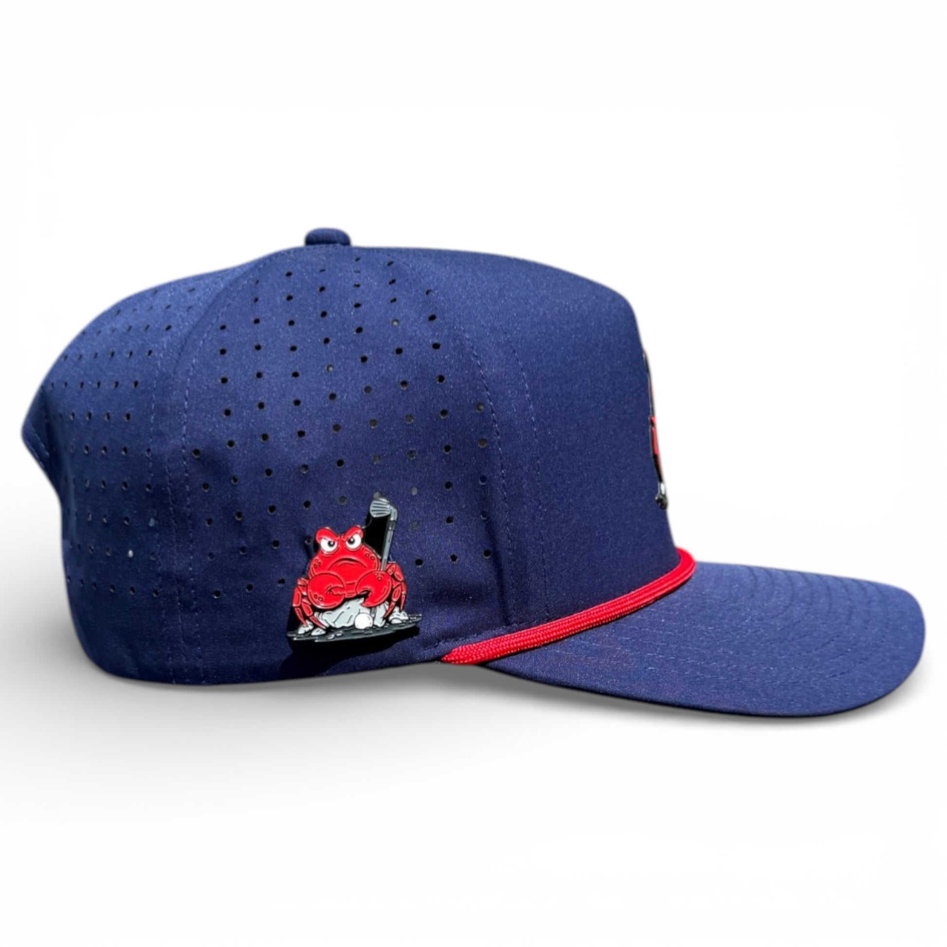 The Crab Trap Golf Hat is a navy blue adjustable snapback cap with red accents, featuring a red cartoon frog holding a baseball bat on the side. It has ventilation holes, a flat brim, and includes a built-in magnetic ball marker holder with marker.