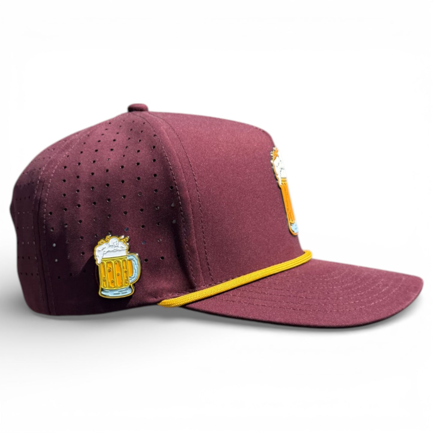 The Cold One Golf Hat is a maroon snapback cap with small perforations, embroidered beer mugs on the front and side, a yellow cord above the brim, and a built-in magnetic holder with marker included. Adjustable and one size fits all.