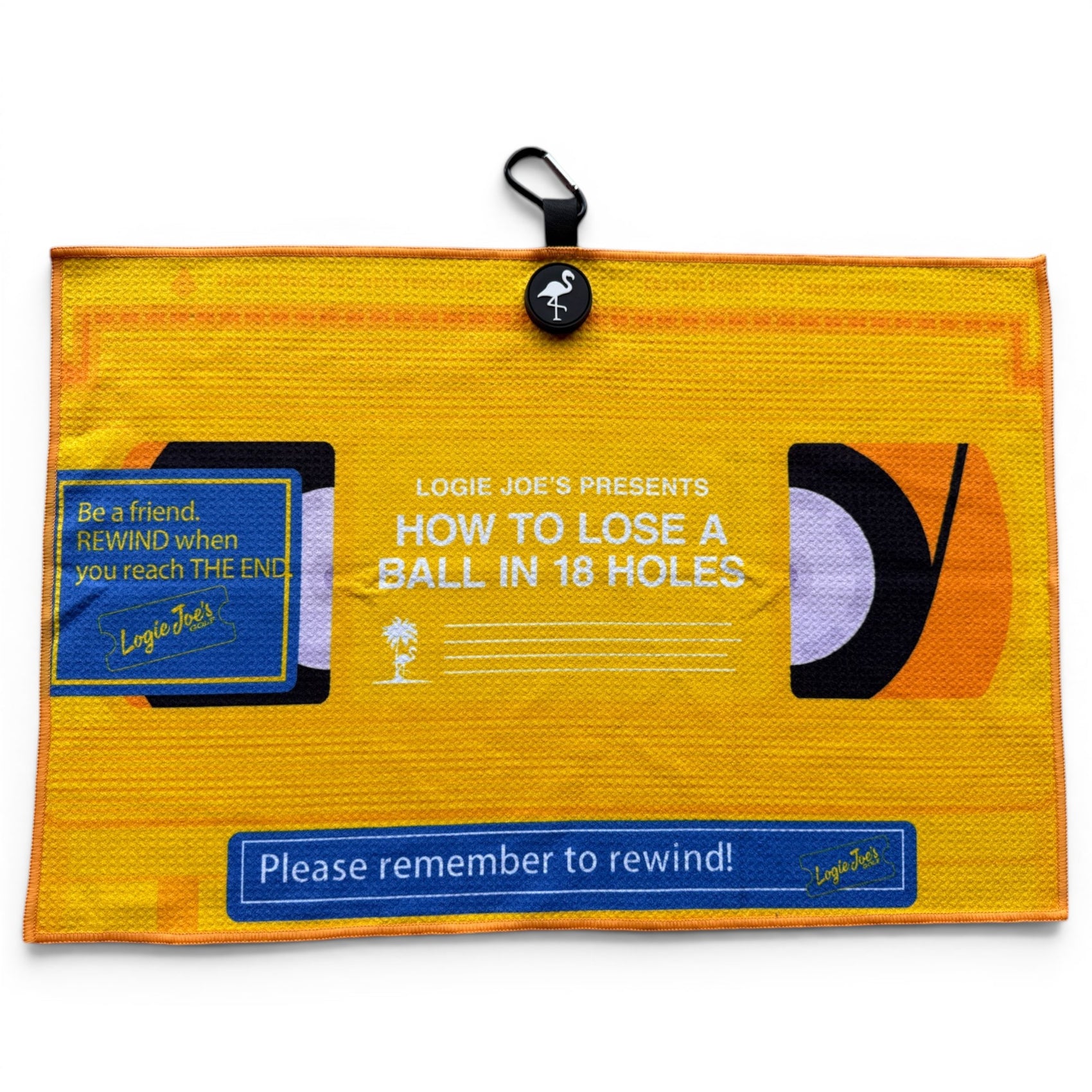 The Block Party Golf Towel is a 24” x 16” yellow microfiber towel styled like a VHS tape, with HOW TO LOSE A BALL IN 18 HOLES text, blue Logie Joe’s labels, and reminders to rewind. Features a magnetic clip and carabiner for easy use.