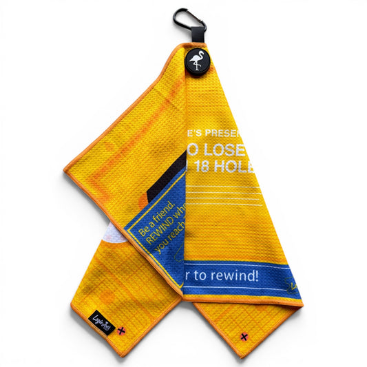 The Block Party Golf Towel is a yellow 24”x16” microfiber towel with a magnetic clip and carabiner, blue and white partial text, plus a small black tag with white text in the bottom left corner.
