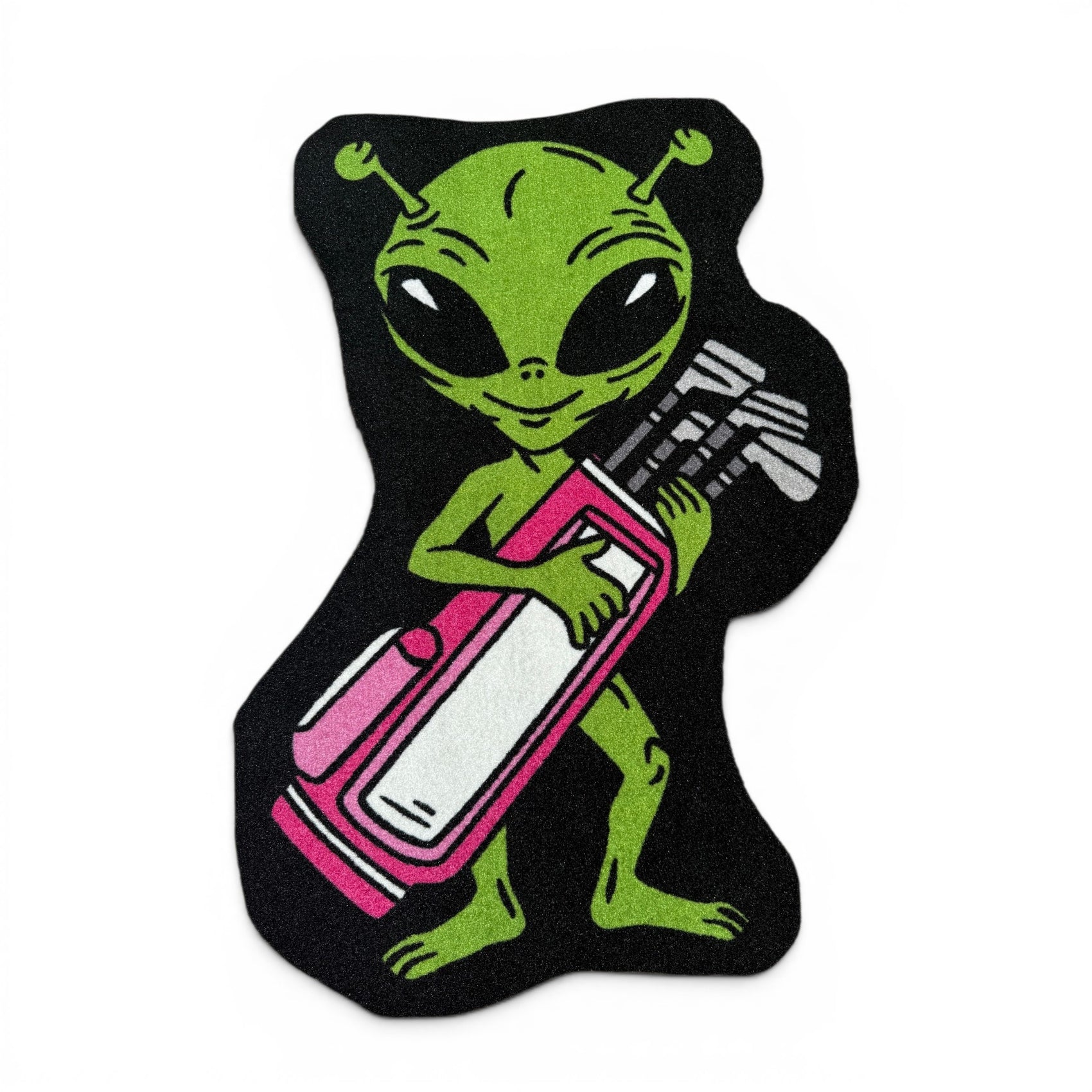 A cartoon green alien holds a pink and white golf bag with clubs, standing on a black background, ready to tee off on the Alien Caddy | Golf Shop Mat | Cart Accessory.