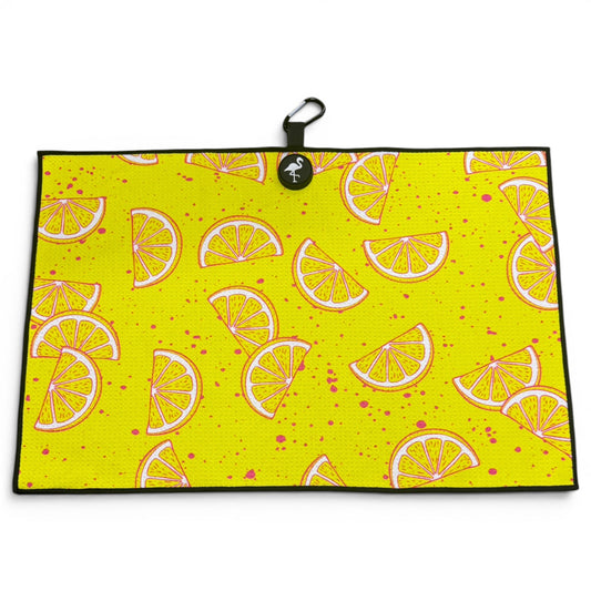 The Main Squeeze Golf Towel is a 24” x 16” yellow microfiber towel with illustrated lemon slices, pink splatters, black border, and comes with a magnetic clip and carabiner—perfect as a premium golf accessory.