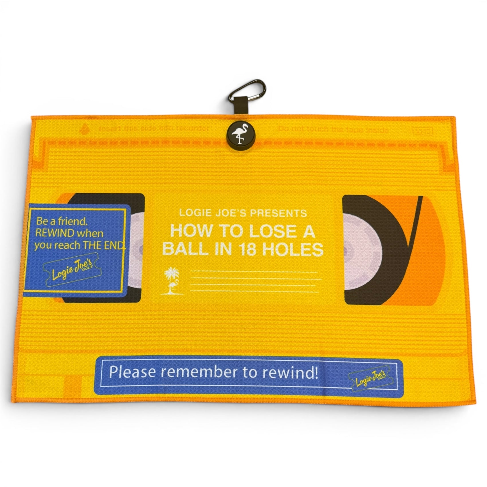 The Block Party Golf Towel (24” x 16” microfiber) features a VHS tape design with the text: Logie Joes Presents: How to Lose a Ball in 18 Holes, and blue labels saying, Be a friend. REWIND when you reach THE END. Includes magnetic clip & carabiner.