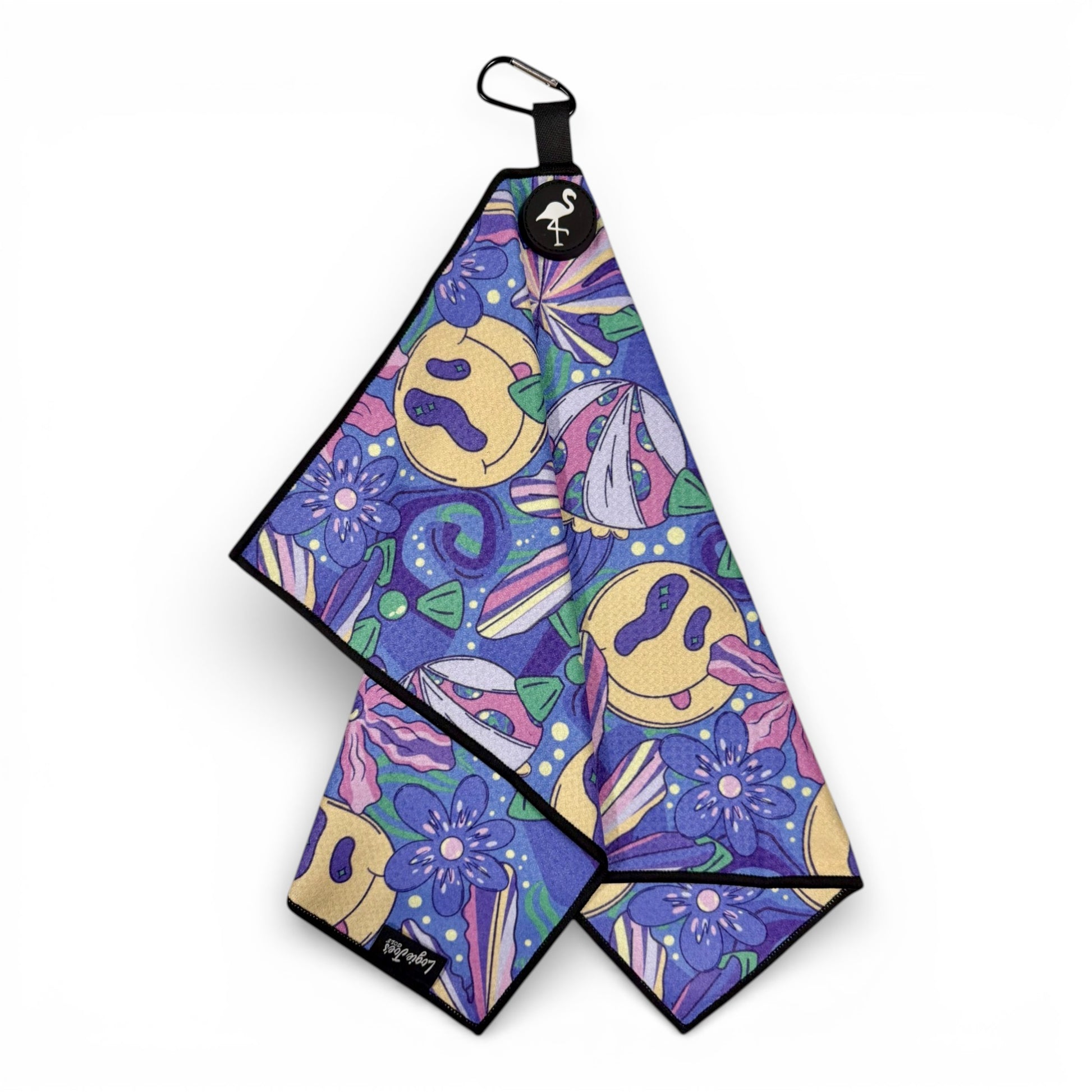 The Purple Haze Golf Towel features a 90s-inspired design with yellow smiley faces, purple flowers, and pastel shapes. This 24 x 16 in premium double-sided microfiber towel includes a black border, magnetic feature, and carabiner clip.