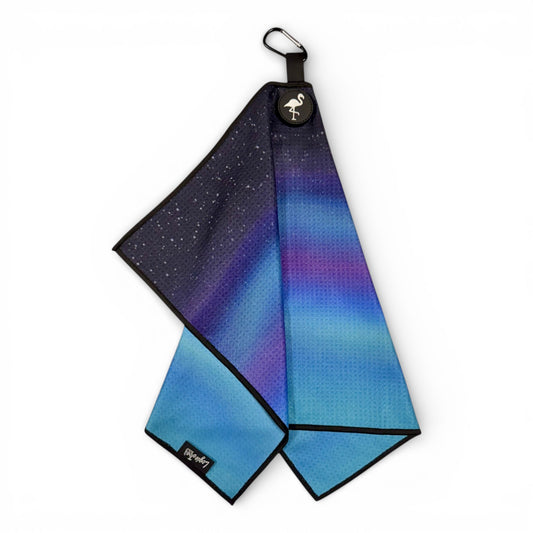 The Northern Lights Golf Towel features a blue and purple aurora-inspired gradient with black trim, double-sided premium microfiber, night sky design with white dots, a flamingo logo tag, magnetic back, and a carabiner clip. Size: 24 x 16 in.