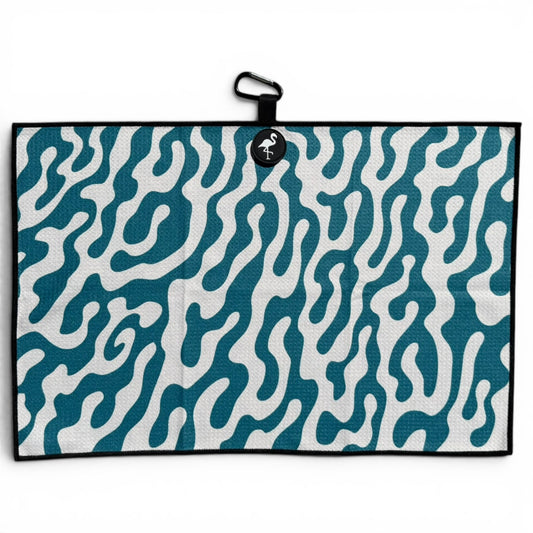 The Coral Bloom Golf Towel is a 24” x 16” microfiber towel in teal and white with an abstract wavy pattern, a black border, a black loop, flamingo tag at the top, plus magnetic clip and carabiner for easy attachment.