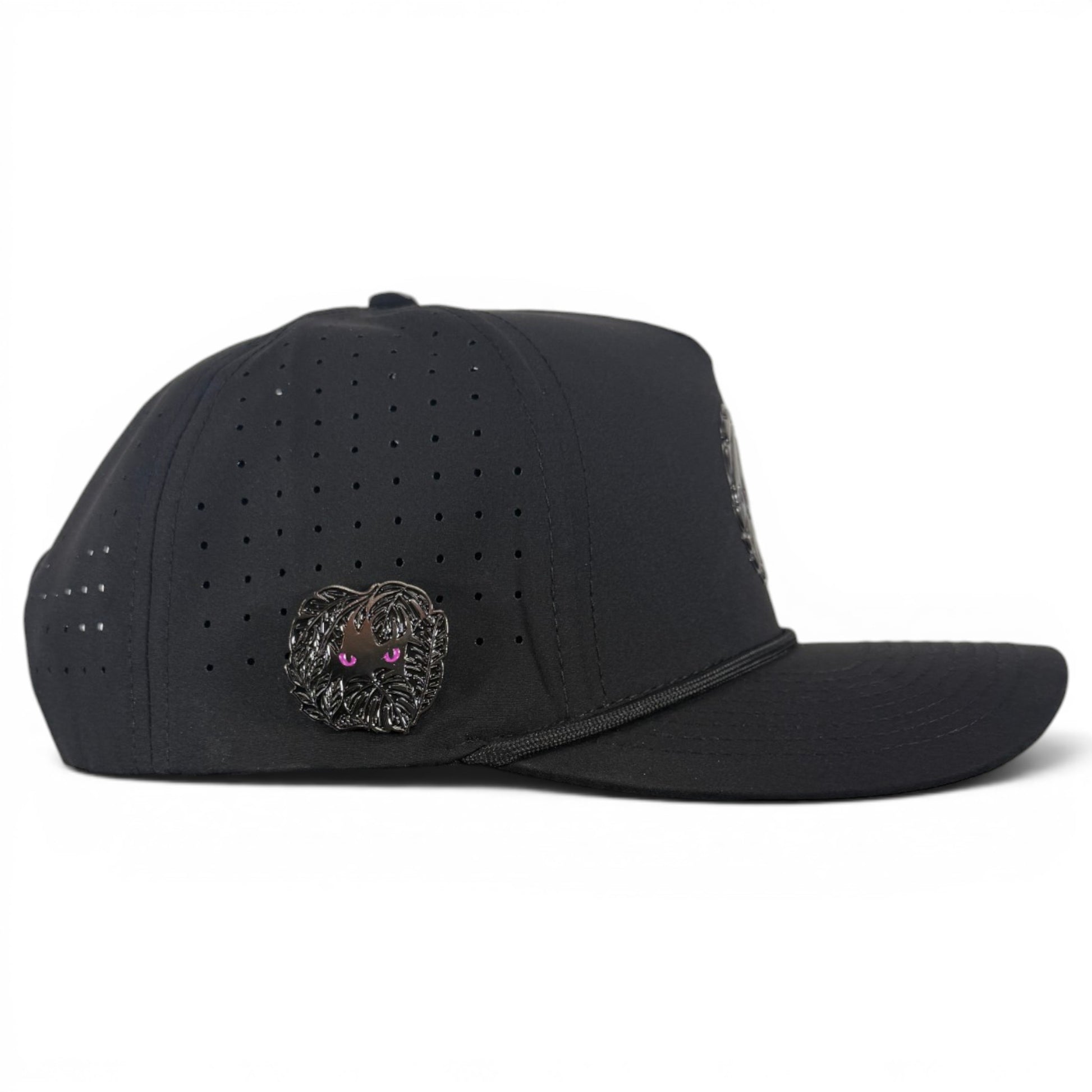 The Night Stalker Golf Hat in Animal Eyes Black is an adjustable snapback cap with a built-in magnetic ball marker holder and included marker, featuring small ventilation holes and a side metallic pin shaped like a furry creature with purple eyes.