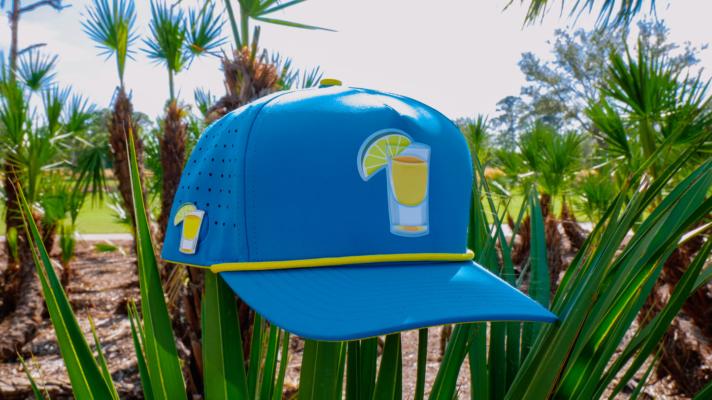 The Tequila and Lime Golf Hat is a blue snapback cap with a lemon drink graphic, yellow trim, built-in magnetic ball marker holder (with marker), shot glass, and adjustable fit—perfect for sunny rounds on the green.