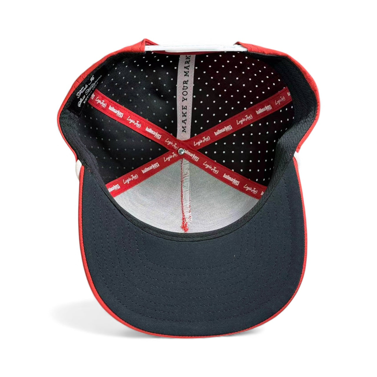 The inside view of the Missing Milk Golf Hat - an adjustable red and black snapback with a built-in magnetic ball marker holder - features a black brim, red lining with white logos, polka-dot fabric, and “MAKE YOUR MARK.” printed inside.