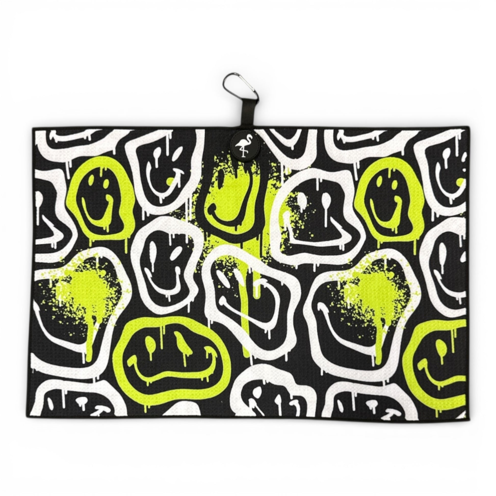 The Drippy Smile Golf Towel (24x16 in) features abstract white and neon yellow drippy smile faces on a black microfiber backdrop, paint splatter accents, and includes a heavy-duty magnetic back plus carabiner clip for easy access.