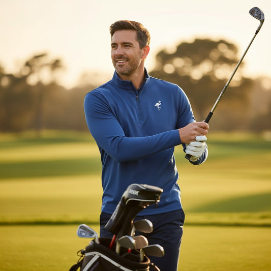 A man smiles on a sunlit golf course, holding a club with his golf bag nearby, while wearing the Unisex Marble Wave Performance Quarter Zip— a lightweight, moisture-wicking golf pullover. Trees frame the background.