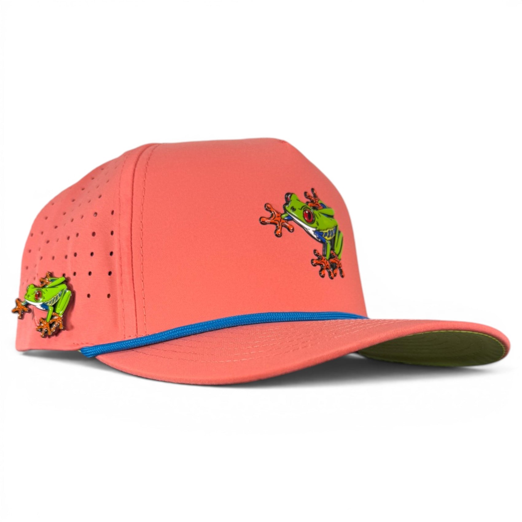 The Tree Frog Golf Hat is a coral pink snapback cap with blue-trimmed brim, embroidered green red-eyed frogs, built-in magnetic ball marker holder with marker included, adjustable fit, and ventilation holes for comfort.