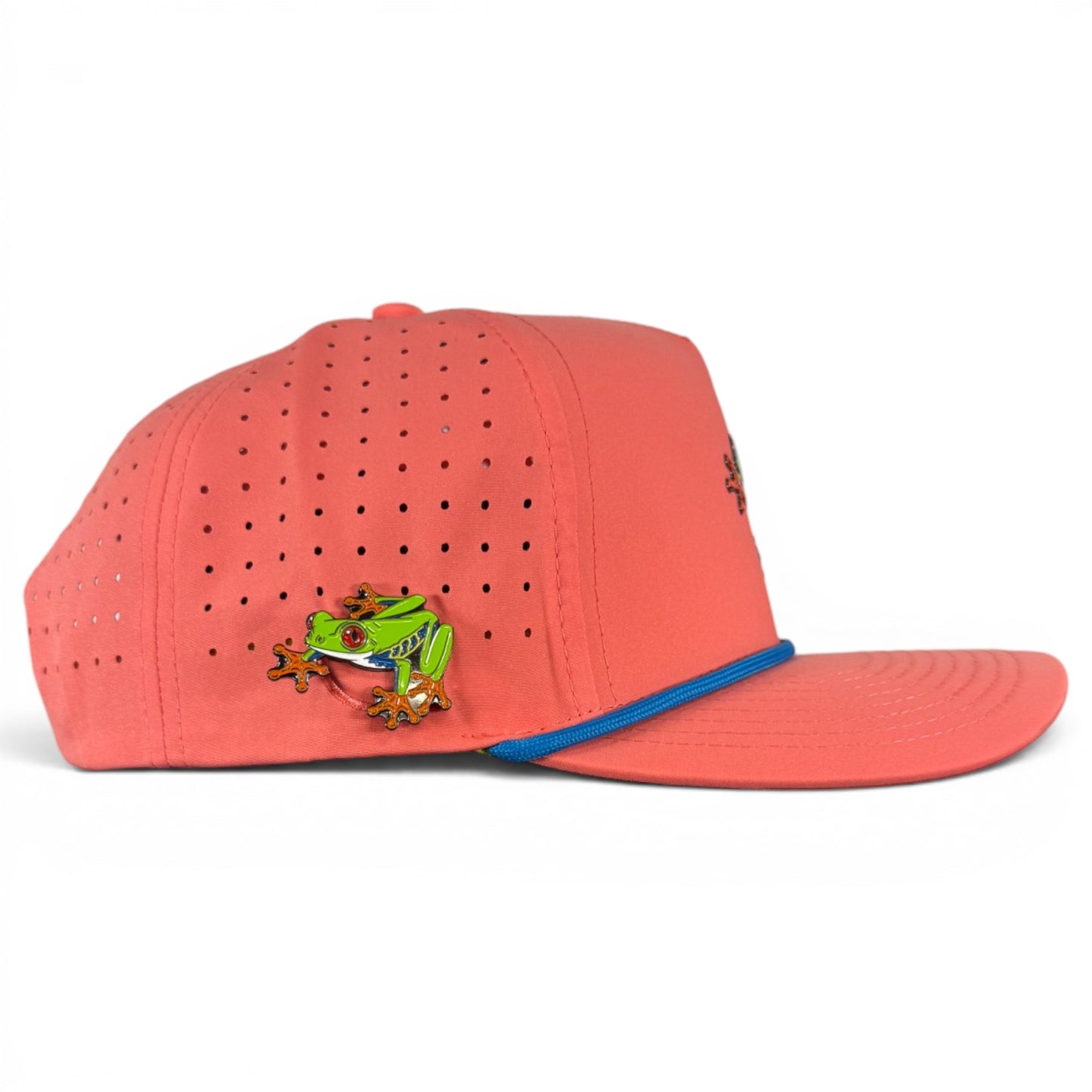 A coral pink Tree Frog Golf Hat (Snapback Cap) with a blue-trimmed brim, colorful frog enamel pin, built-in magnetic ball marker holder (marker included), and red eyes, displayed against a white background.